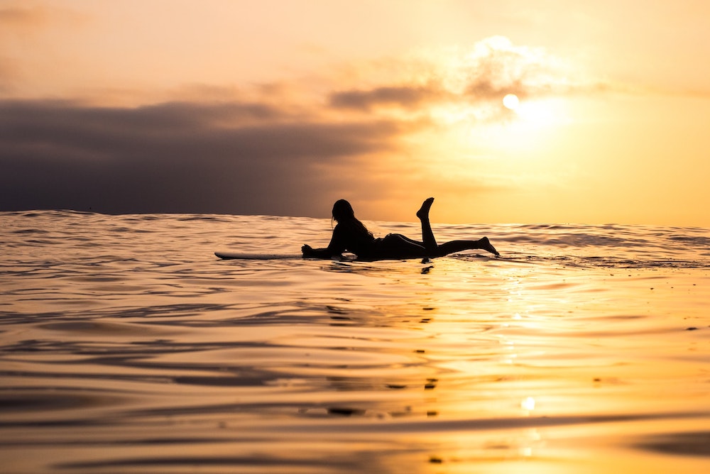 A surfer lying on a surfboard in sunset